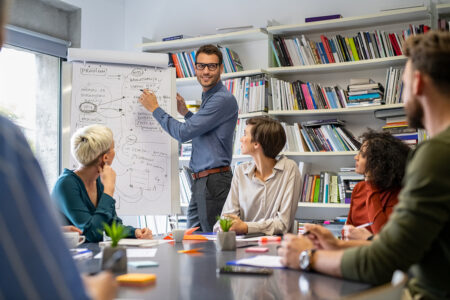 Confident businessman giving a presentation in casual office. Leader briefing his creative business team with annual goals. Mid business man training multiethnic businesspeople in conference room.